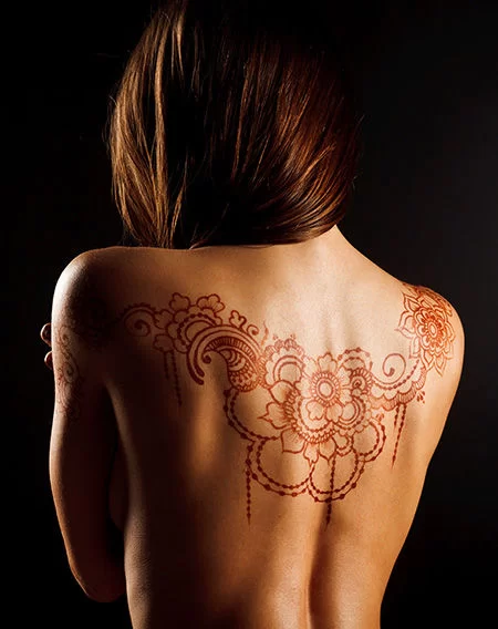 Intricate floral henna tattoo art across a woman's back for professional bridal and body art.